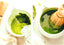 Matcha green tea powder being whisked in a white bowl with a wooden whisk.